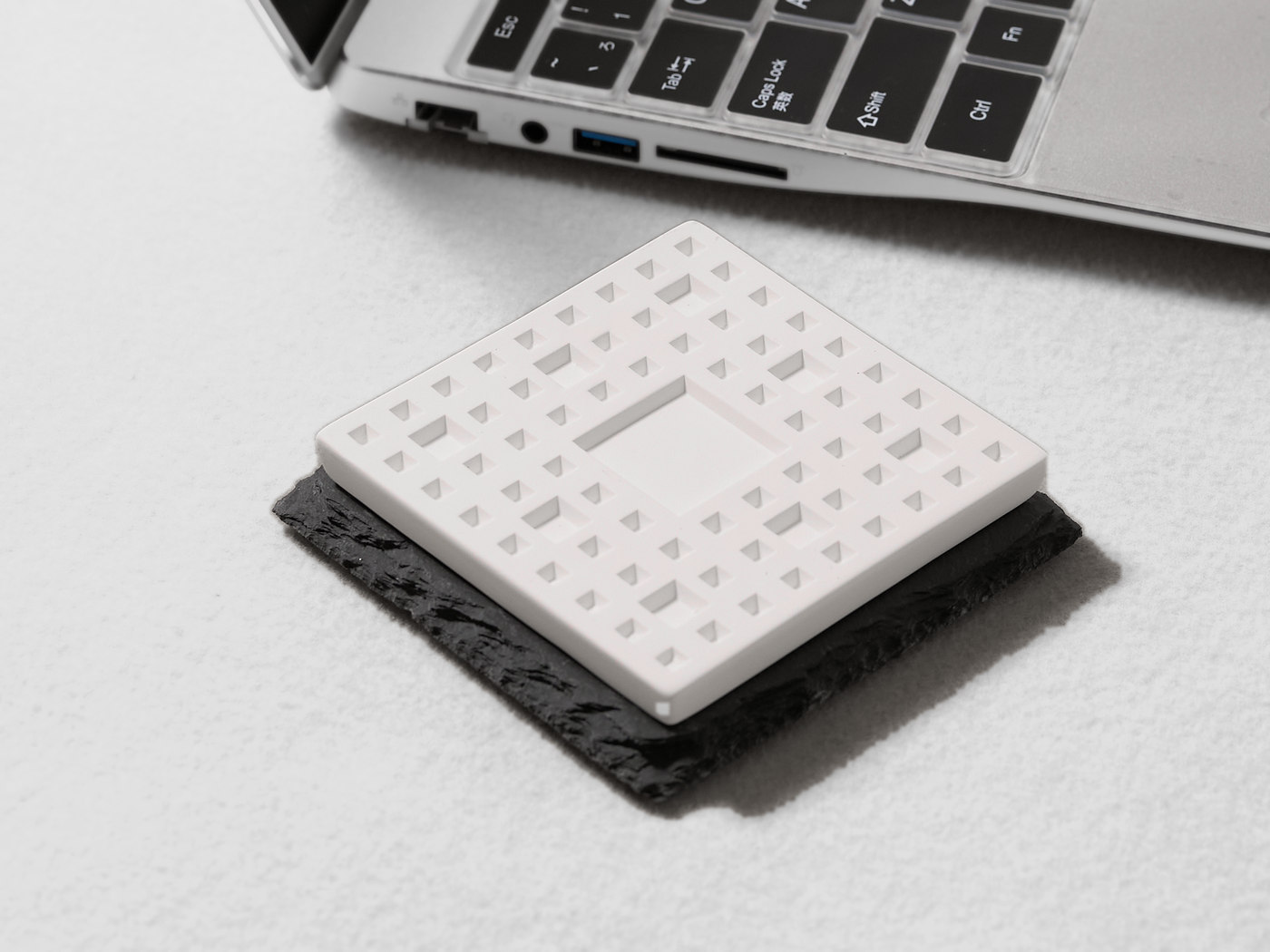 ノートパソコンの手前に置かれた、黒いスレート台座と白い陶器のアロマストーン。